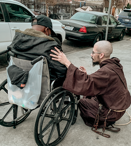 Friar praying with a man in a wheelchair