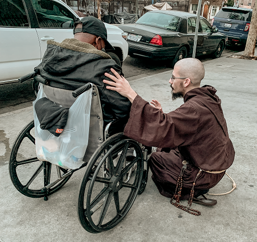 Friar praying with a man in a wheelchair